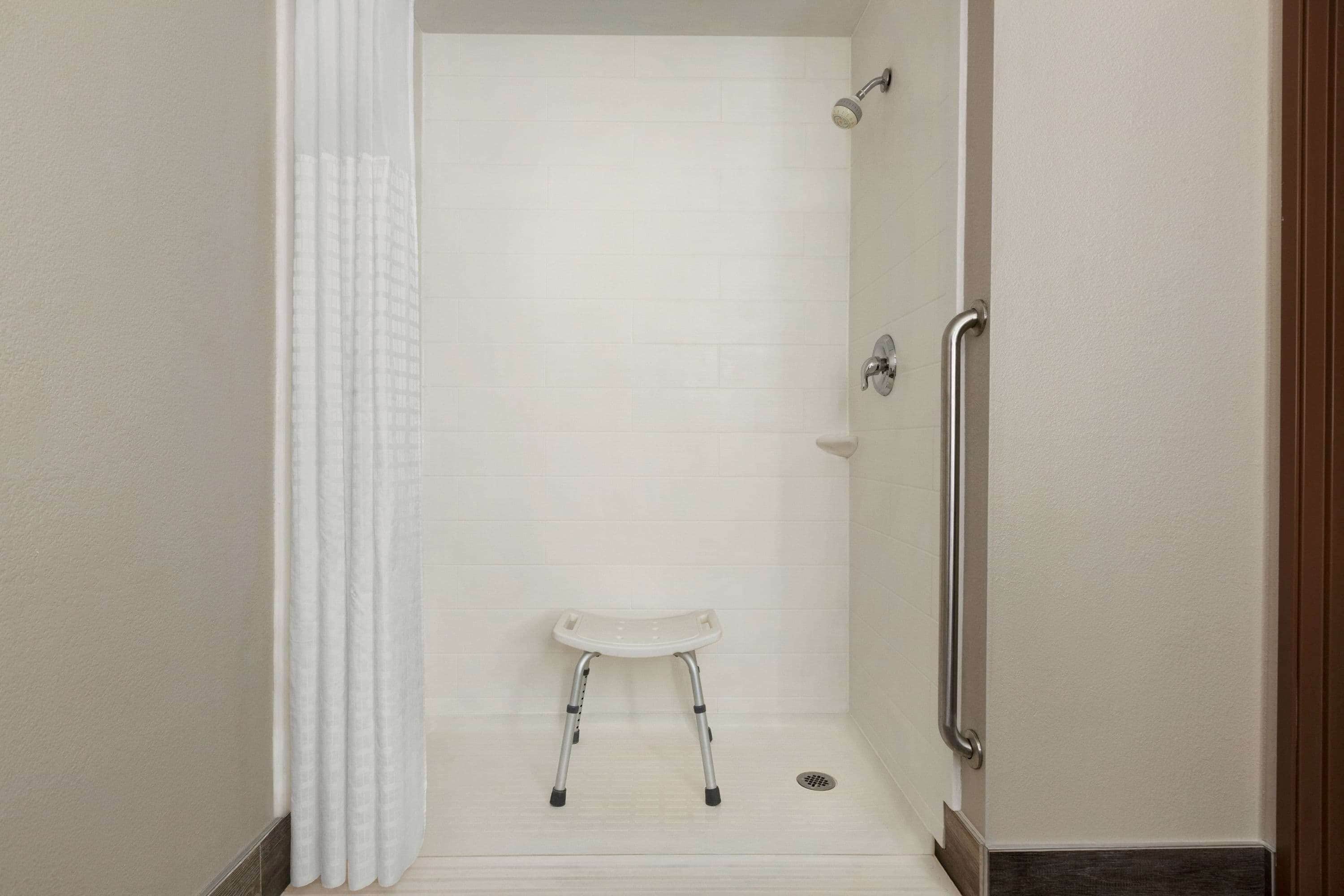 A shower area with a white shower seat and grab bars.
