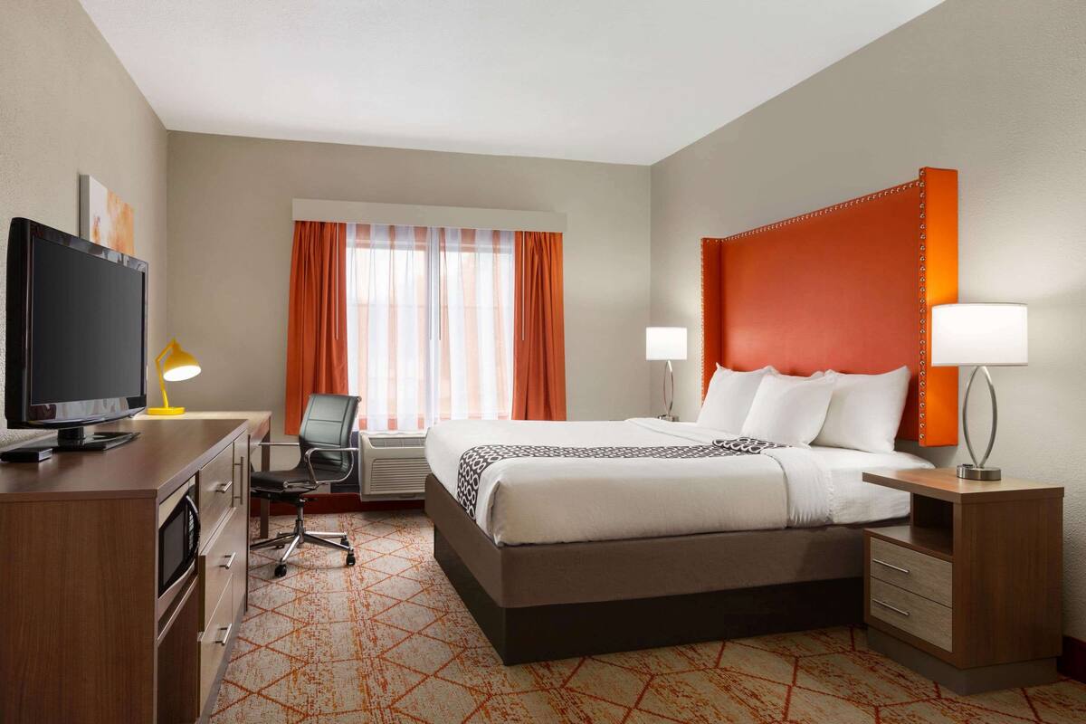 Habitación de hotel con cama, escritorio, televisor y dos lámparas de noche.