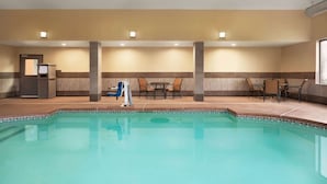 An indoor swimming pool with a tiled edge, surrounded by seating areas and a reception desk. - La Quinta Inn & Suites by Wyndham Lackawanna (Buffalo)