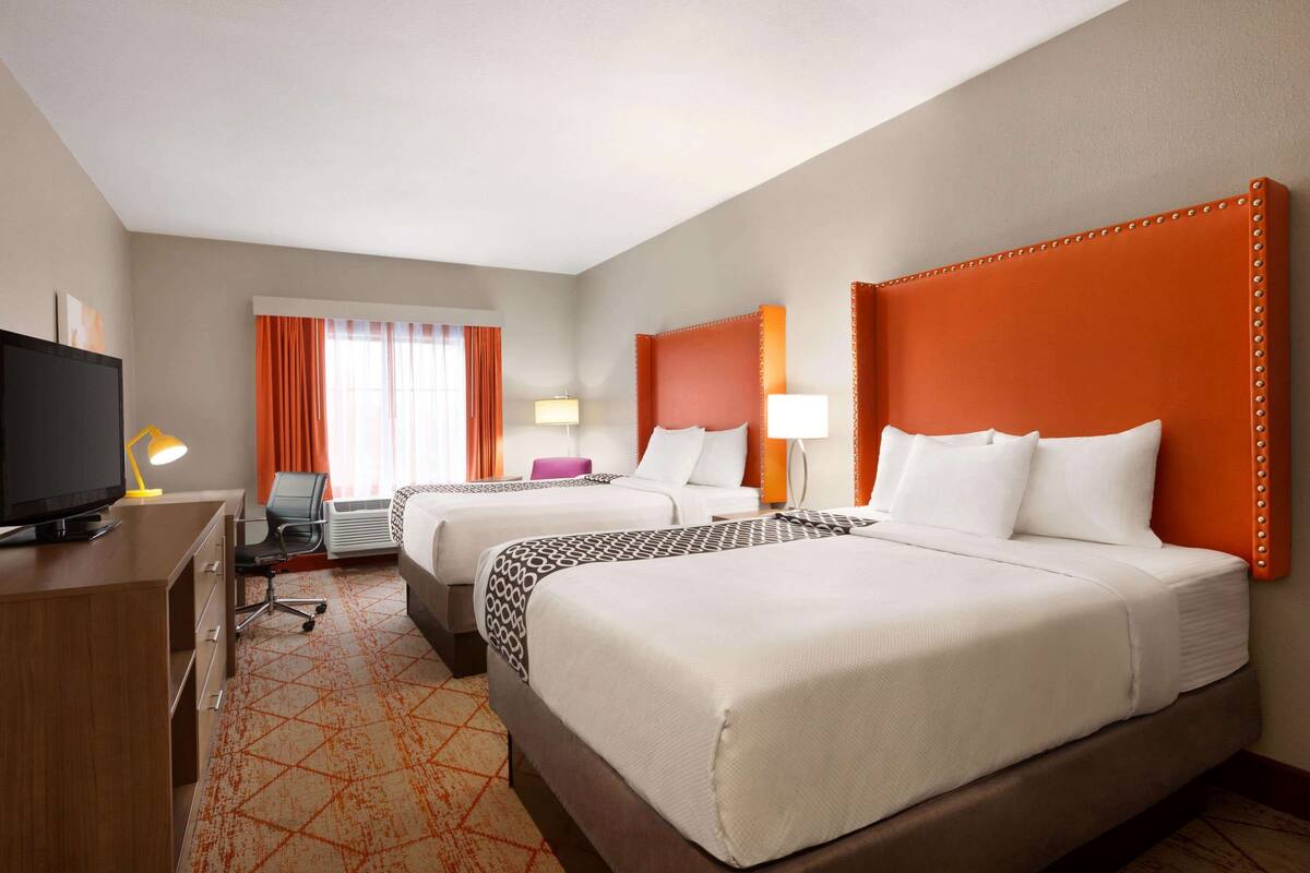 Habitación de hotel con dos camas, un escritorio, un televisor y una silla.