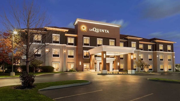 A multi-story hotel with a prominent 'LA QUINTA' sign, featuring a modern architectural design with a covered entrance and a parking lot in front. - La Quinta Inn & Suites by Wyndham Lackawanna (Buffalo)