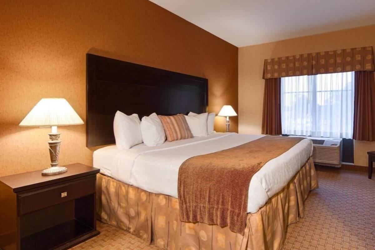 Habitación de hotel con una cama grande, dos lámparas de noche, una ventana con cortinas y un aire acondicionado de pared.