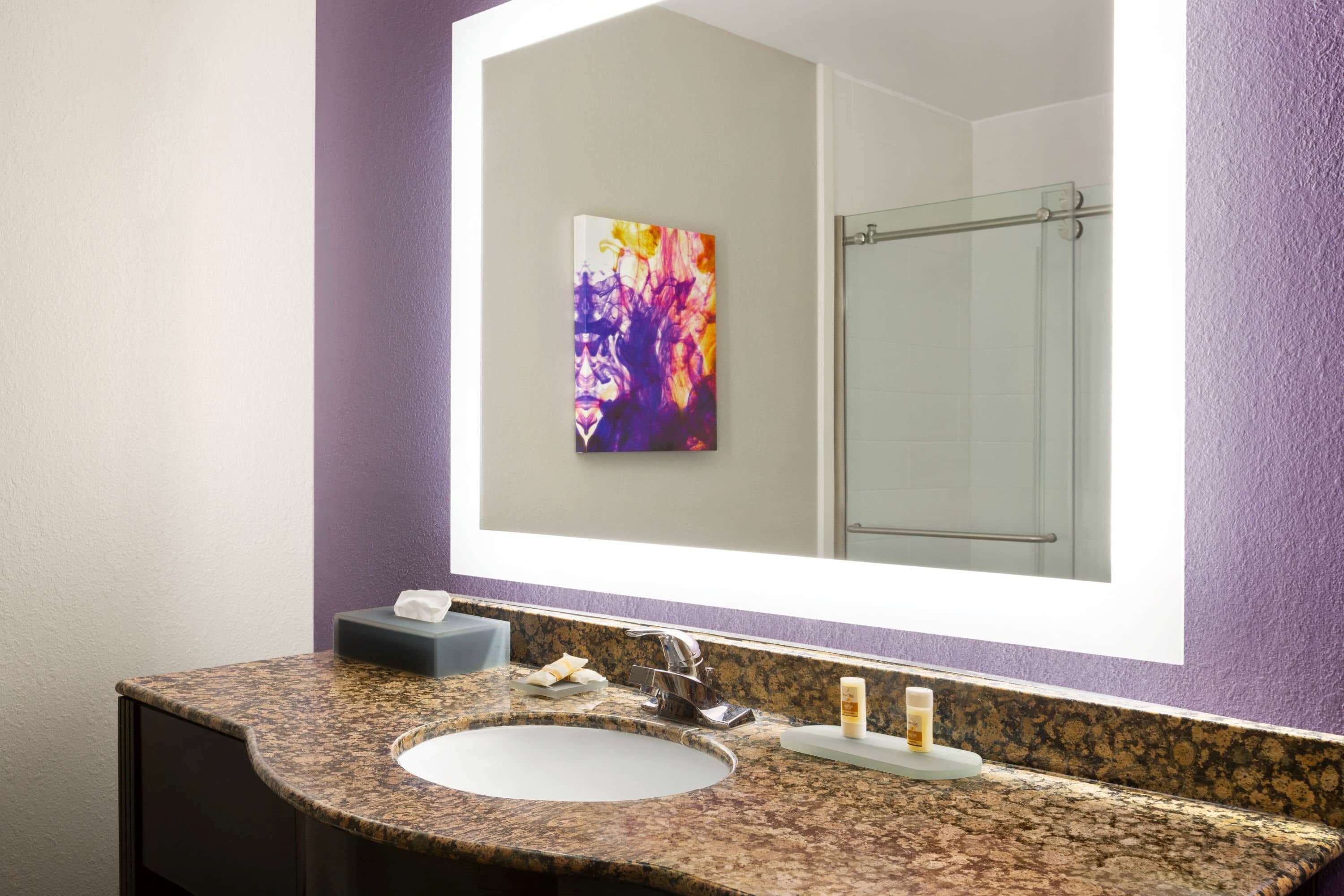 A bathroom with a granite countertop sink, a mirror, and a glass shower enclosure.