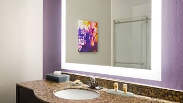 A bathroom with a granite countertop sink, a mirror, and a glass shower enclosure.