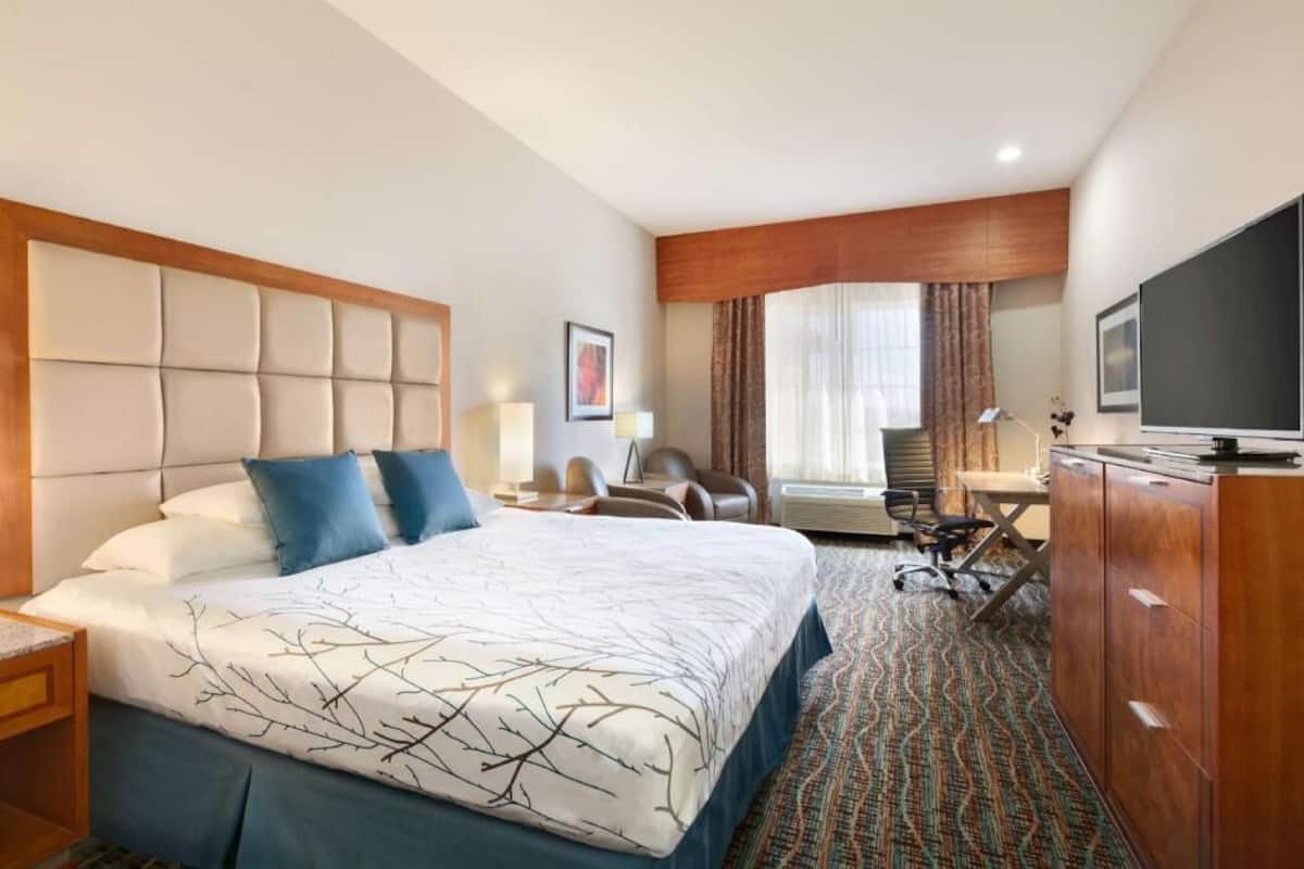 A hotel room with a large bed, a desk, a chair, a television, and a wardrobe.