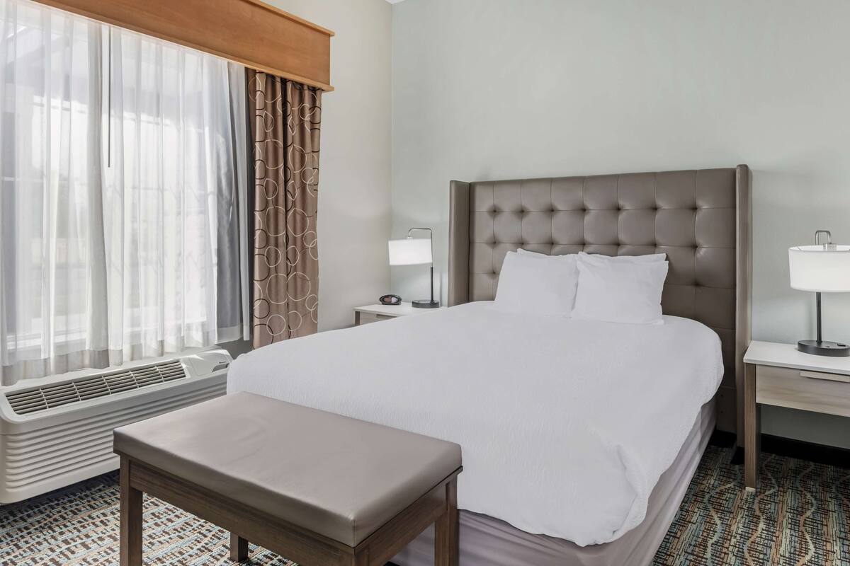A hotel room with a large bed, a bedside table with a lamp, a window with curtains, and a radiator.