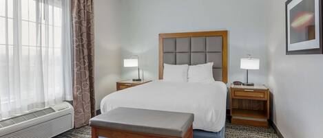 A hotel room with a bed, two bedside tables with lamps, a bench, a window with curtains, and a wall-mounted picture.