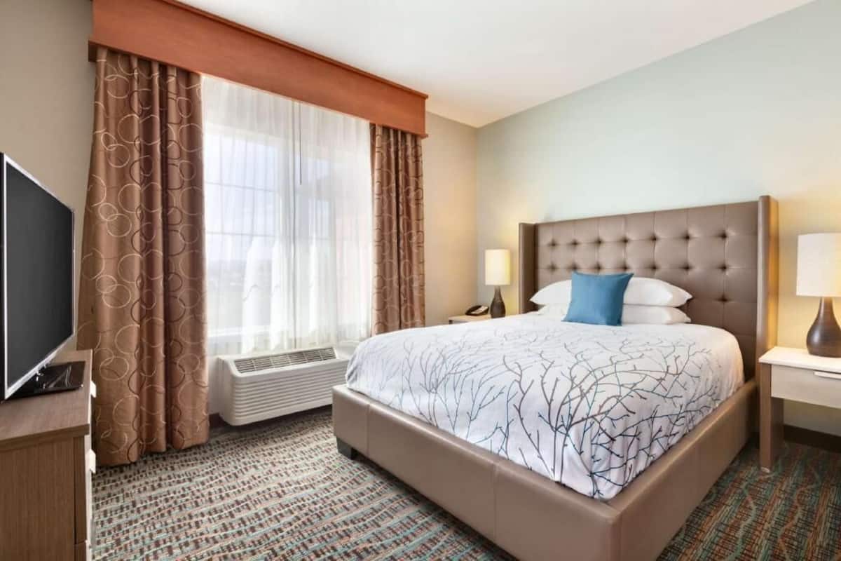 A hotel room with a large bed, a television, a heater, and a window with curtains.