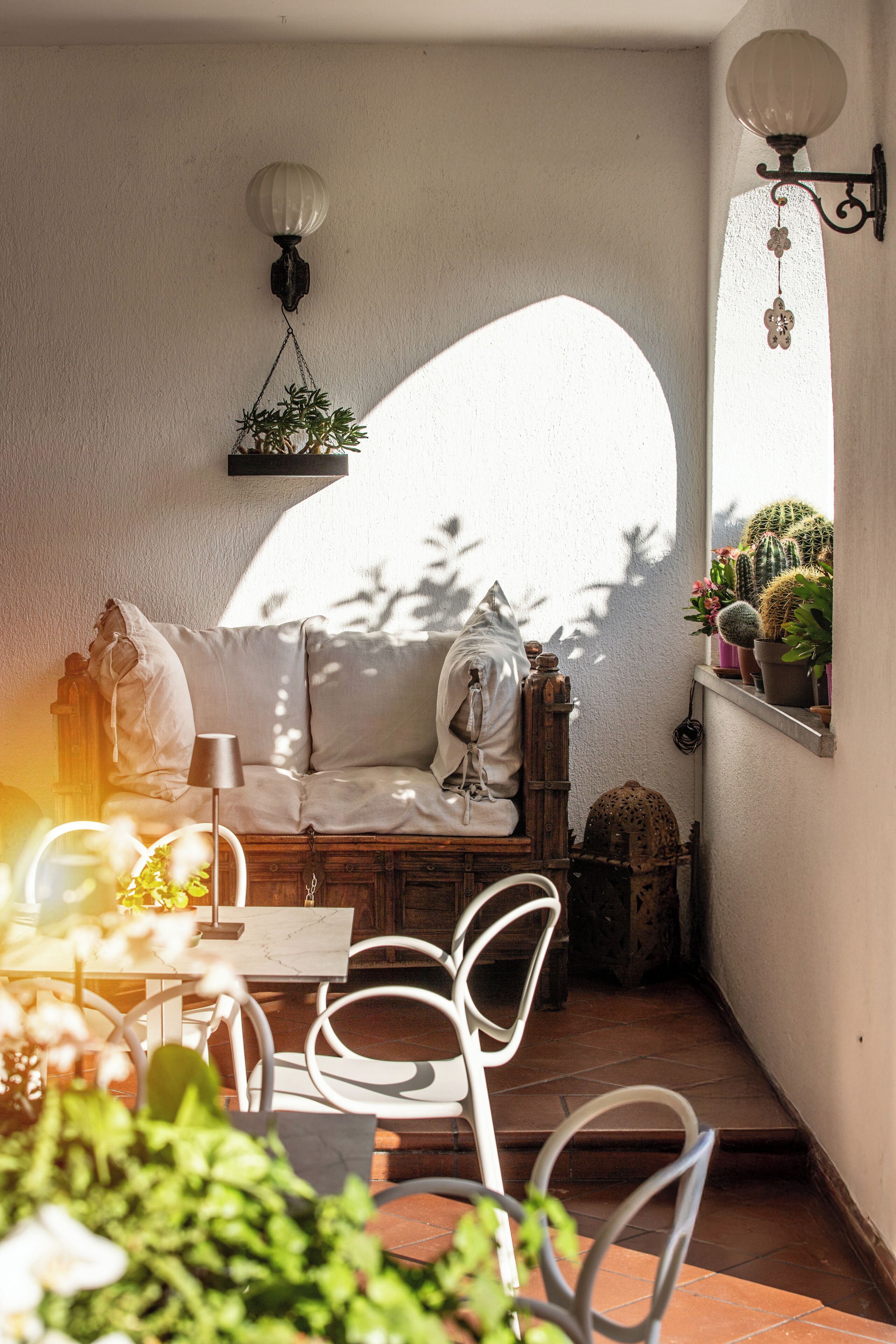 A cozy patio with a white sofa, a table, chairs, and potted plants.