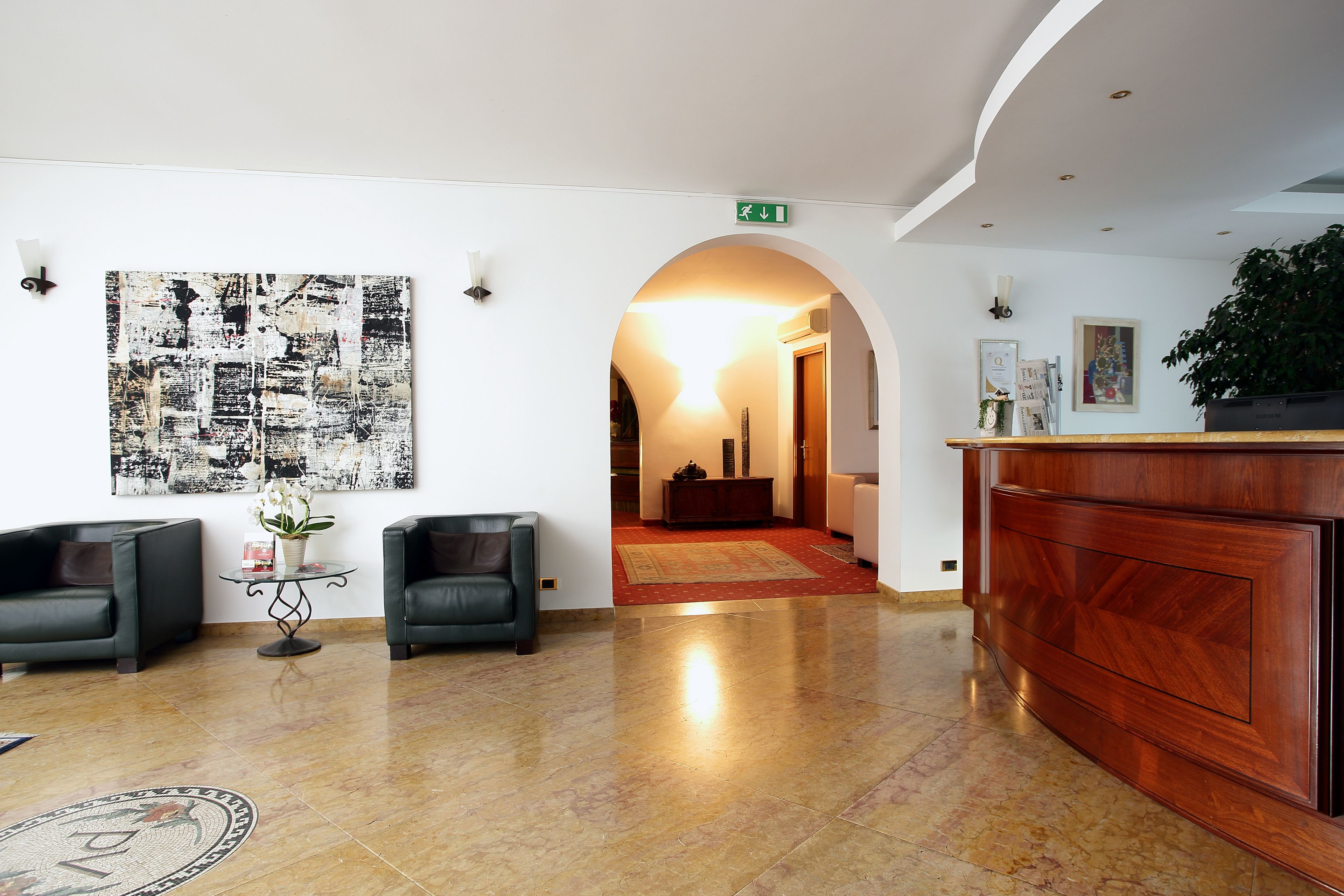 A lobby with a reception desk, two armchairs, a coffee table, and a large abstract painting on the wall.