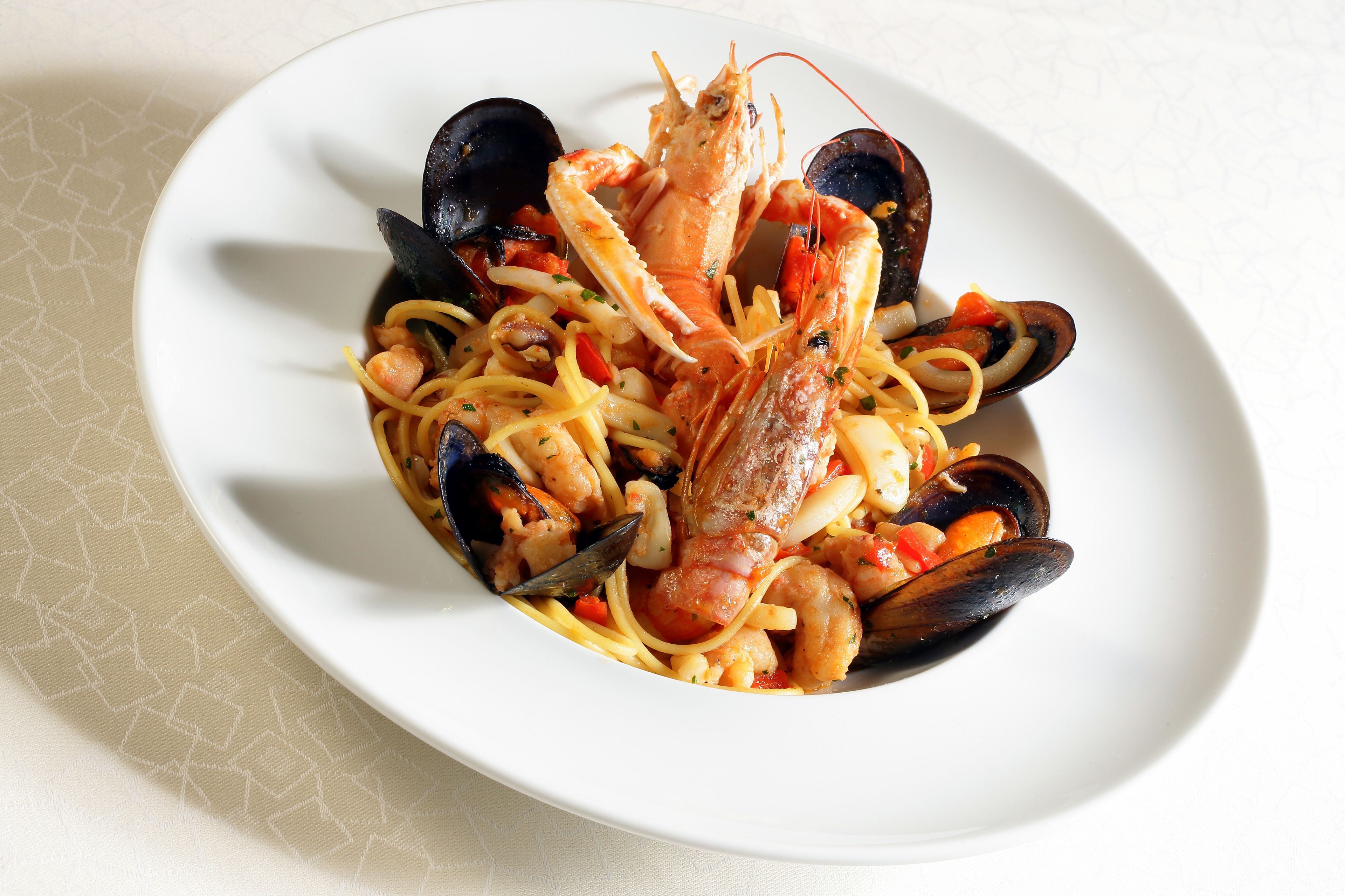 Un plat de pâtes aux fruits de mer servi dans une assiette blanche.
