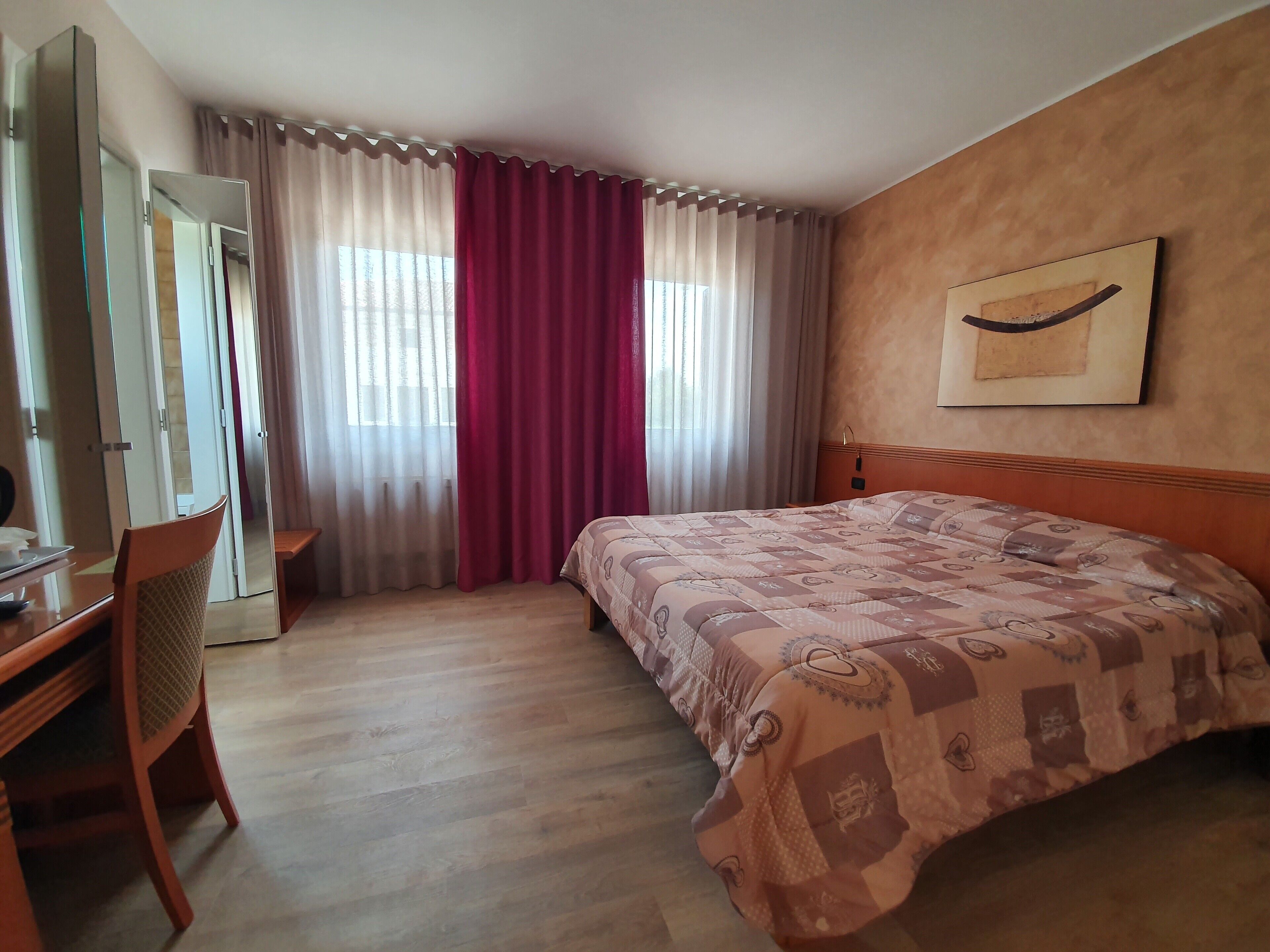 Habitació d'hotel amb un llit, escriptori, cadira i finestra amb cortines.