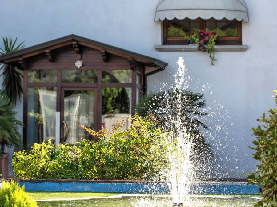 Un bâtiment agrémenté d’une fontaine, une petite construction dotée d’un toit et d’une fenêtre ornée de fleurs.