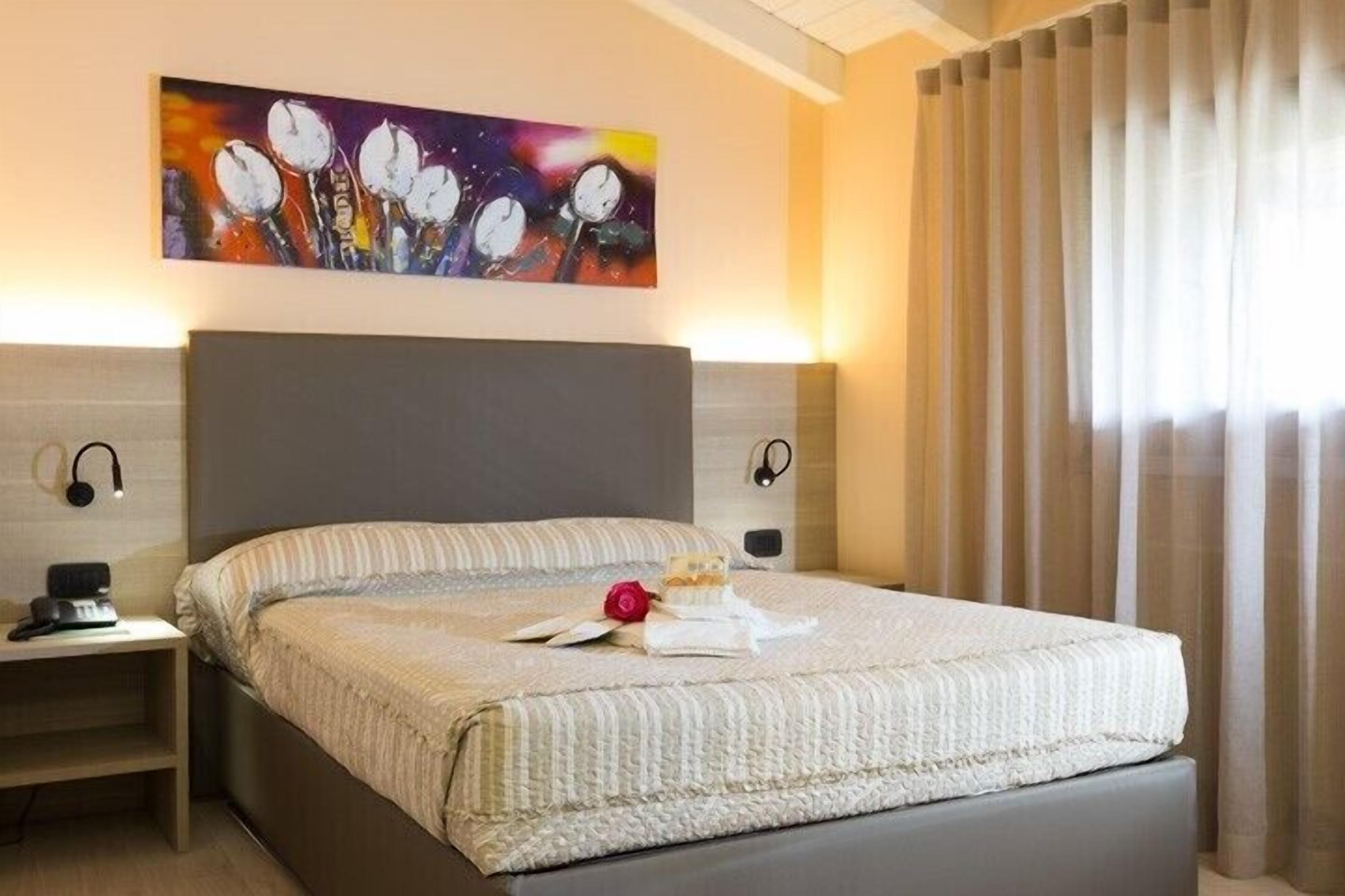 Una cama bien hecha con un edredón a rayas, una mesita de noche con una lámpara y un cuadro sobre la cama.