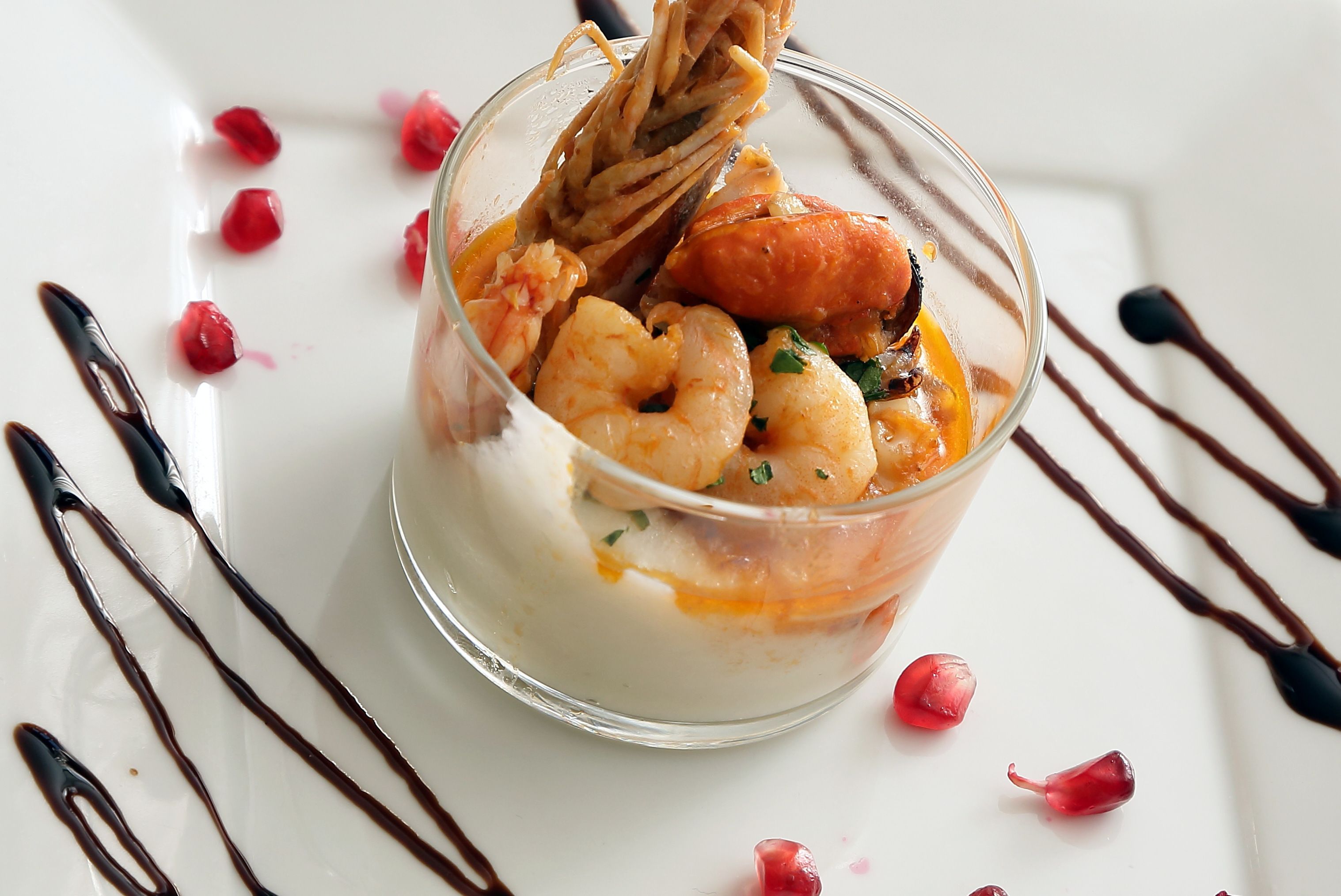 Un dessert composé de crevettes, d’un fruit et d’une sauce, servi dans un verre transparent sur une assiette blanche.