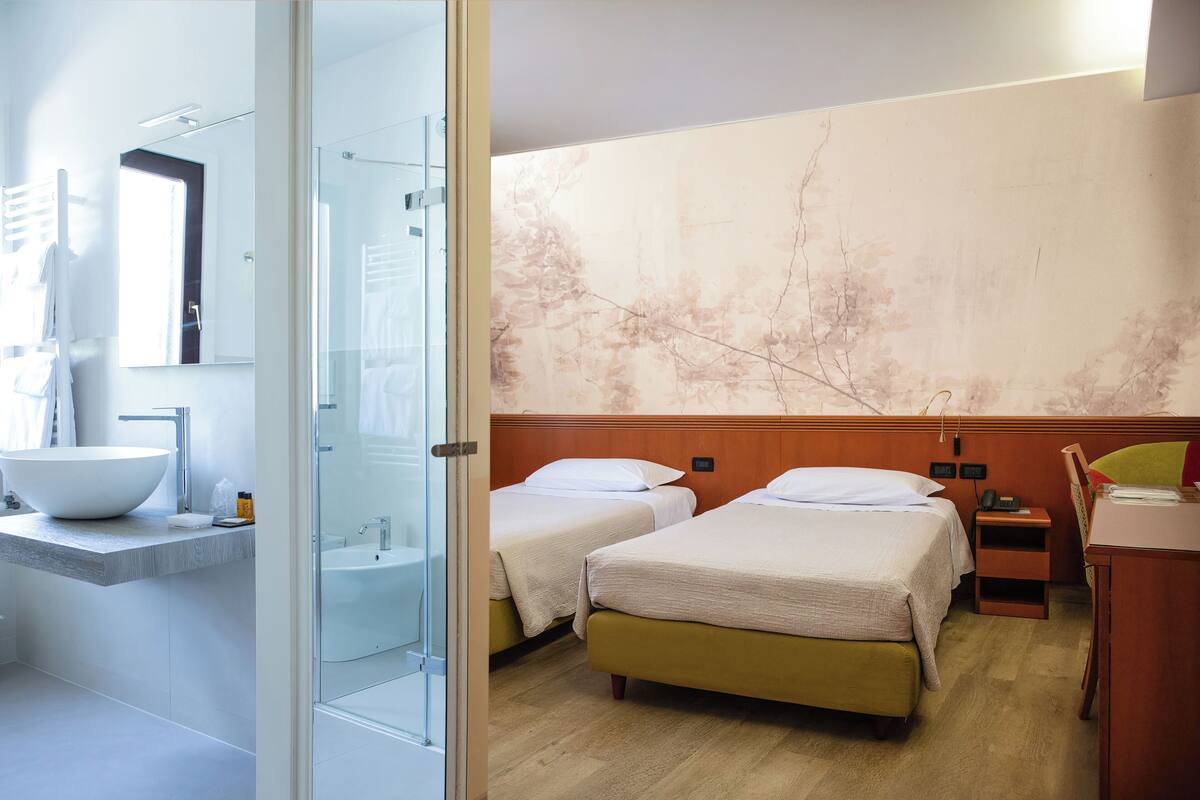 Een hotelkamer met een groot badkamermeubel, een douche, twee bedden, een houten hoofdeinde, een kleine tafel en een stoel.