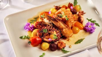 A rectangular plate with a dish of octopus, potatoes, and cherry tomatoes, garnished with herbs and flowers.