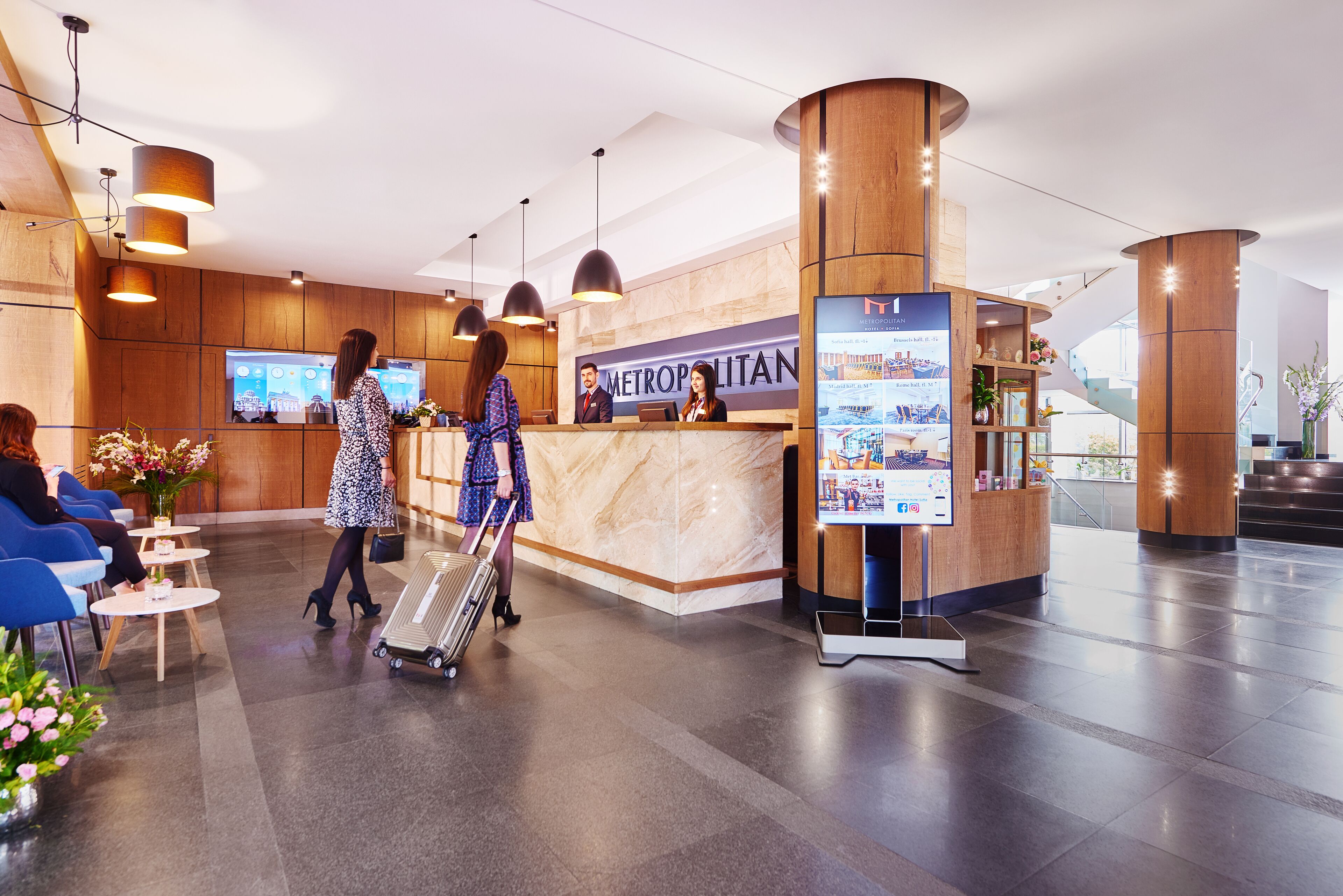 Un moderno vestíbulo de hotel con mostrador de recepción, zona de estar y quiosco de información digital.