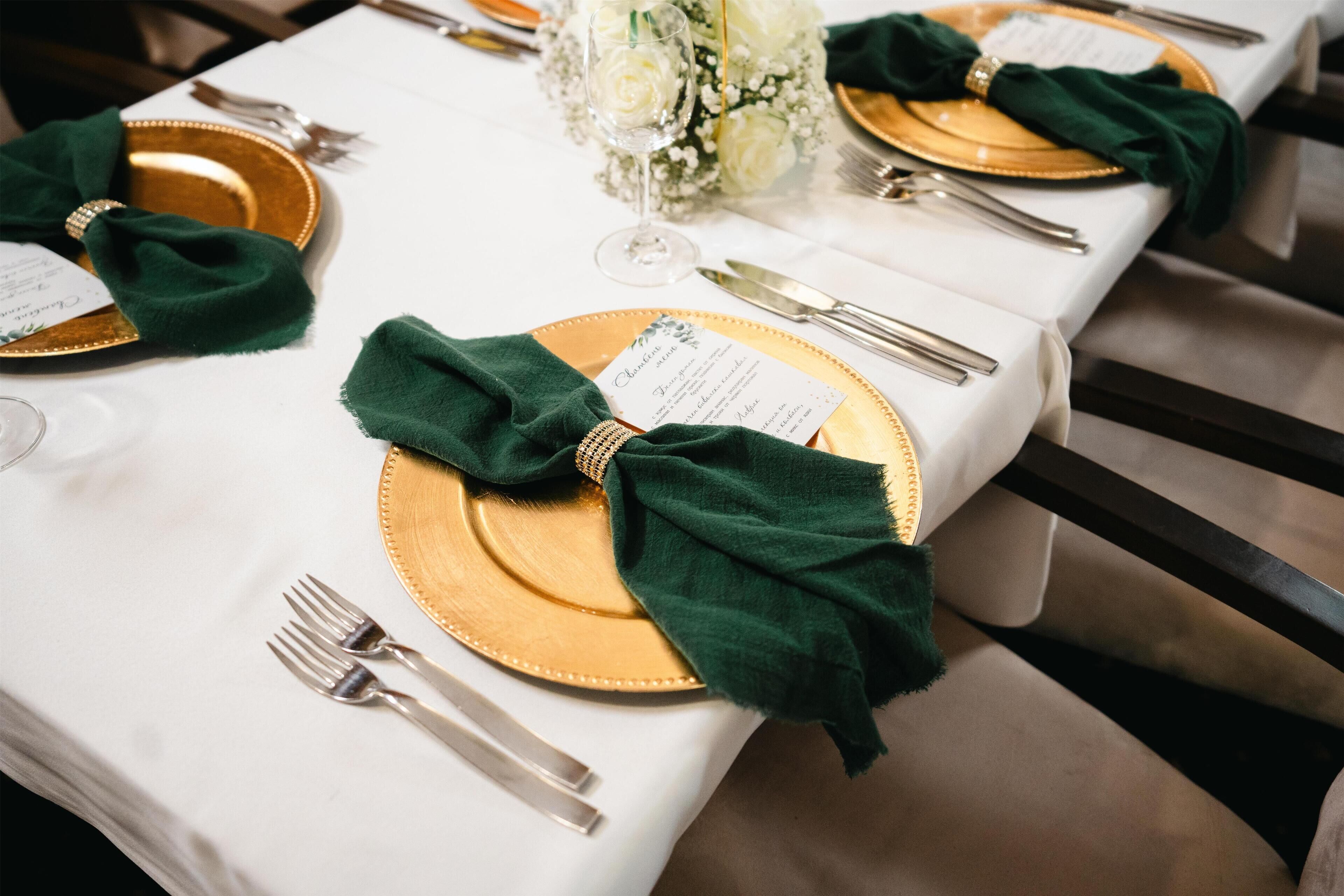 Una mesa dispuesta con vajilla dorada y verde, incluyendo platos, cubiertos y servilletas, con una tarjeta de menú en cada puesto.