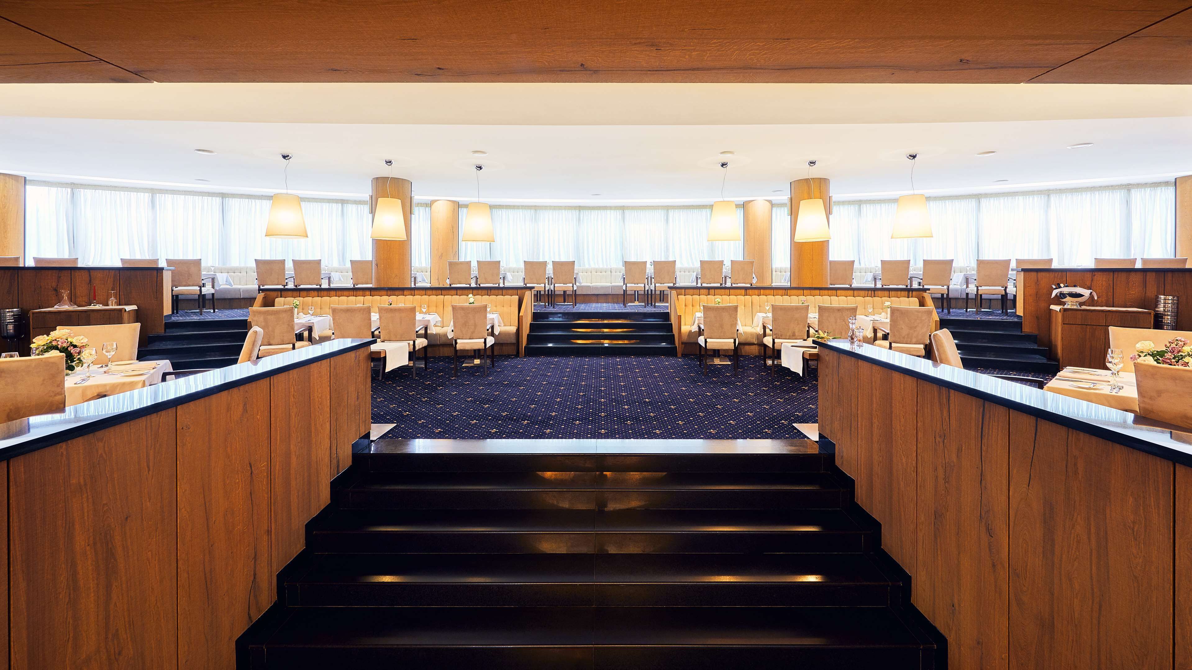 Un vestíbulo de hotel con una escalera central, zonas de estar y una recepción.