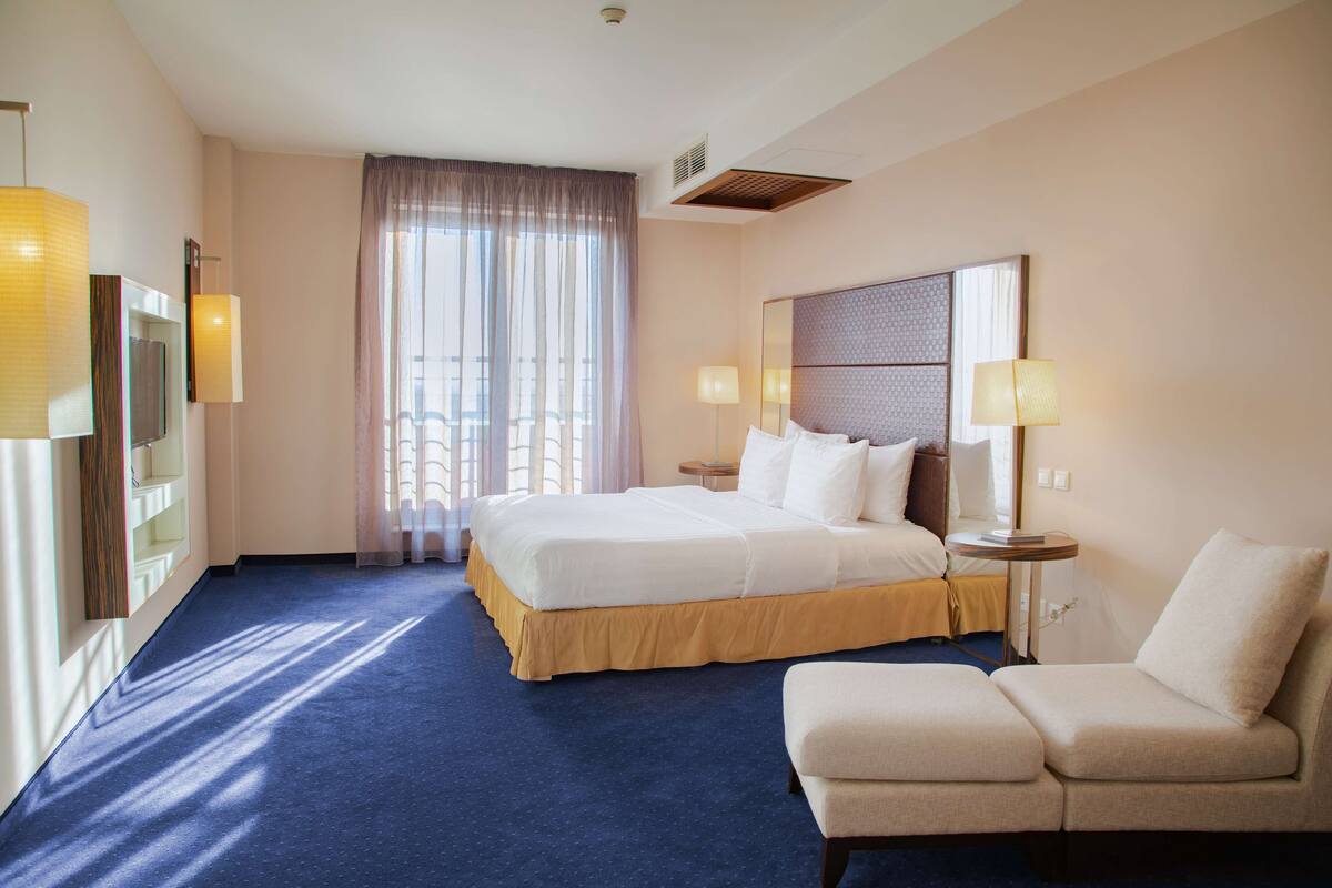 A hotel room with a large bed, a sofa, a desk, and a window with curtains.