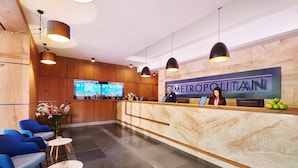 A hotel reception area with a marble counter, blue chairs, and a digital screen displaying the hotel name. - Metropolitan Hotel Sofia, a member of Radisson Individuals (Sofia)