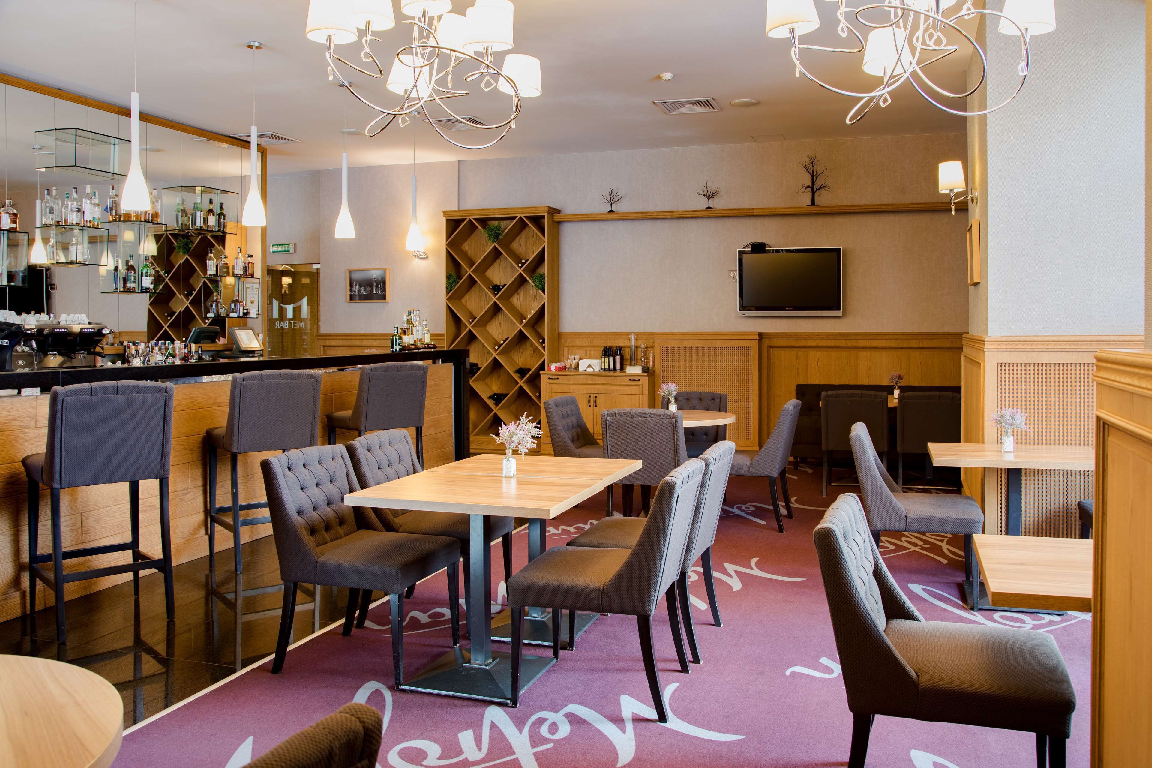 Un restaurant doté d’un bar, de plusieurs types de sièges, notamment des tables et des banquettes, et d’un téléviseur fixé au mur.