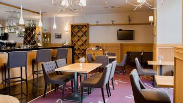 Un restaurant doté d’un bar, de plusieurs types de sièges, notamment des tables et des banquettes, et d’un téléviseur fixé au mur.