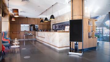 A modern hotel lobby with a reception desk, seating area, and a staircase.