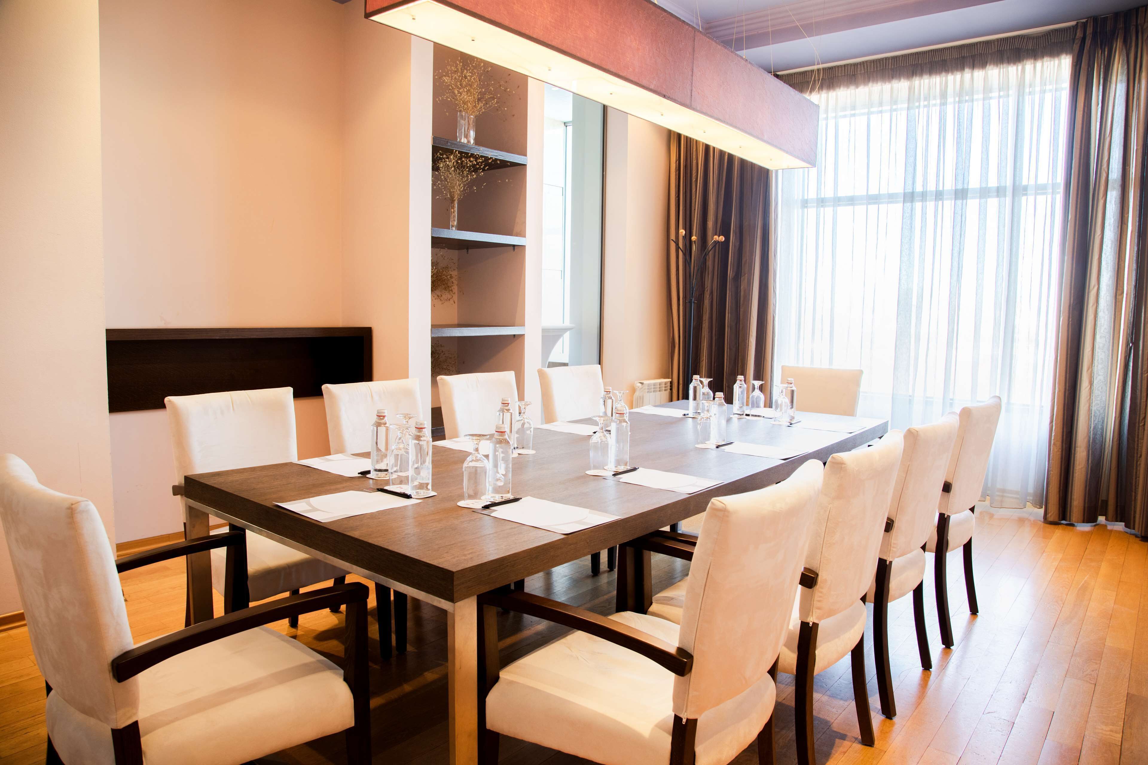 A conference room with a long table, white chairs, and a modern chandelier.