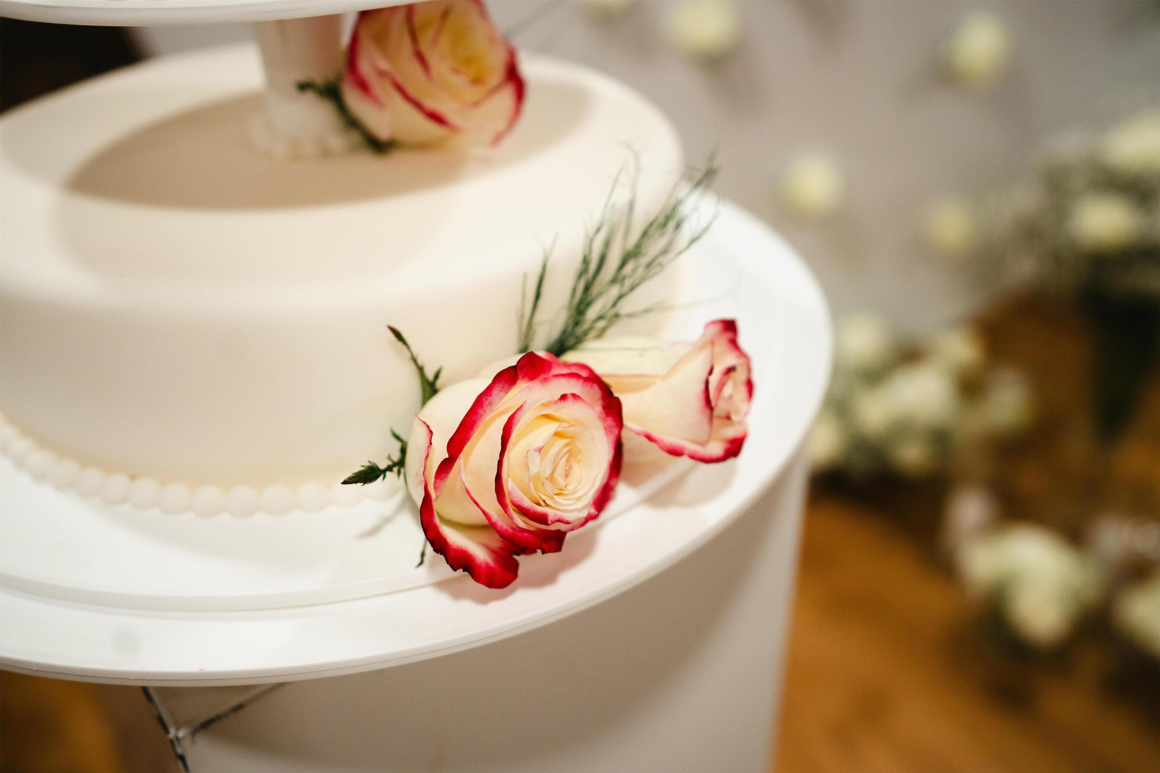 A tiered white cake with red and white roses on top.