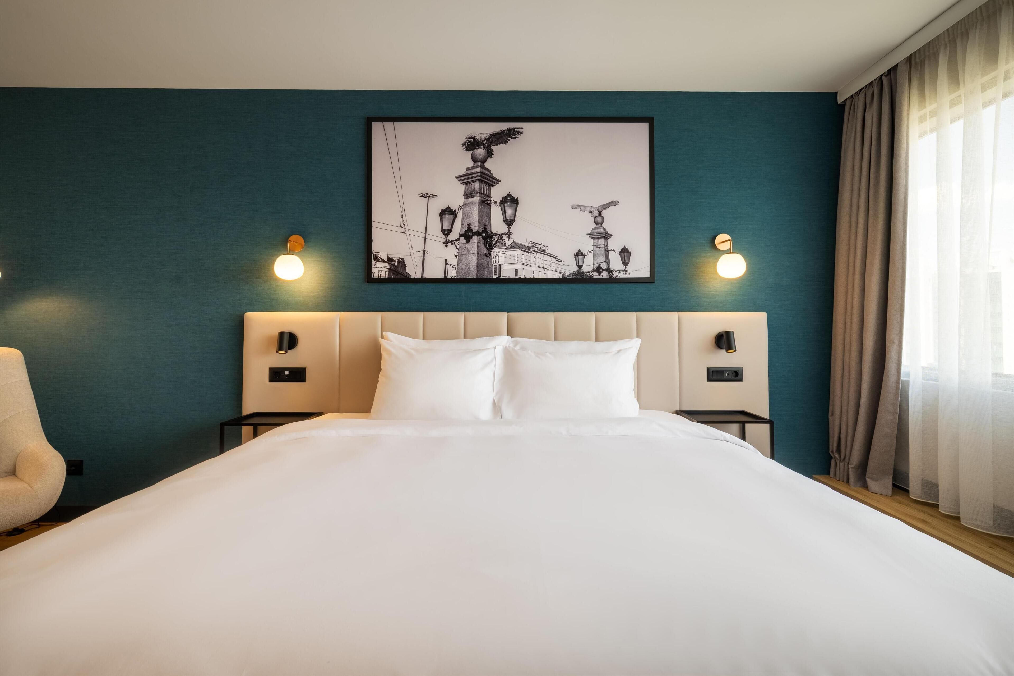 A hotel room with a large bed, two bedside tables, a headboard, and a framed picture on the wall.