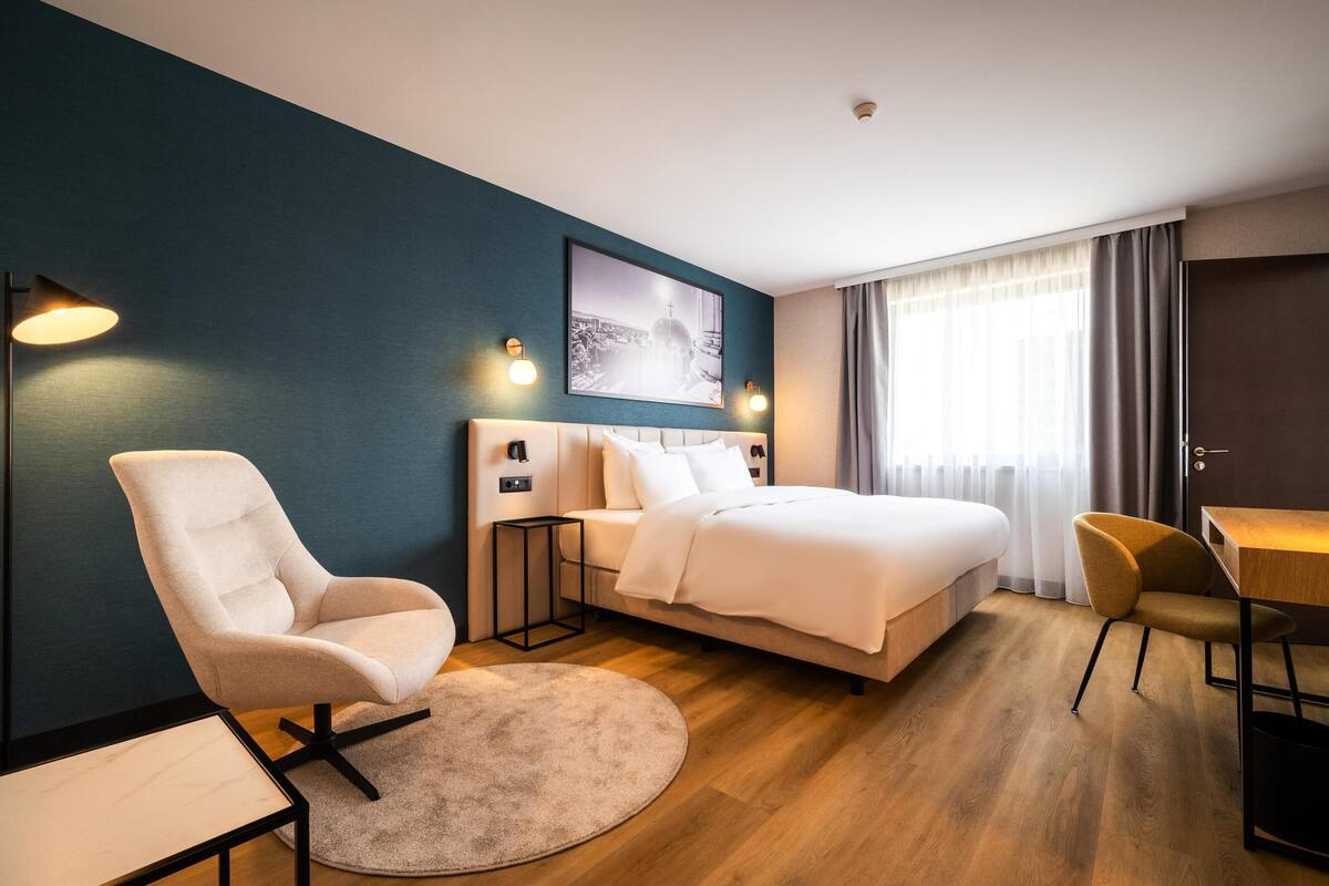 A modern hotel room with a bed, two chairs, a desk, and a round rug.