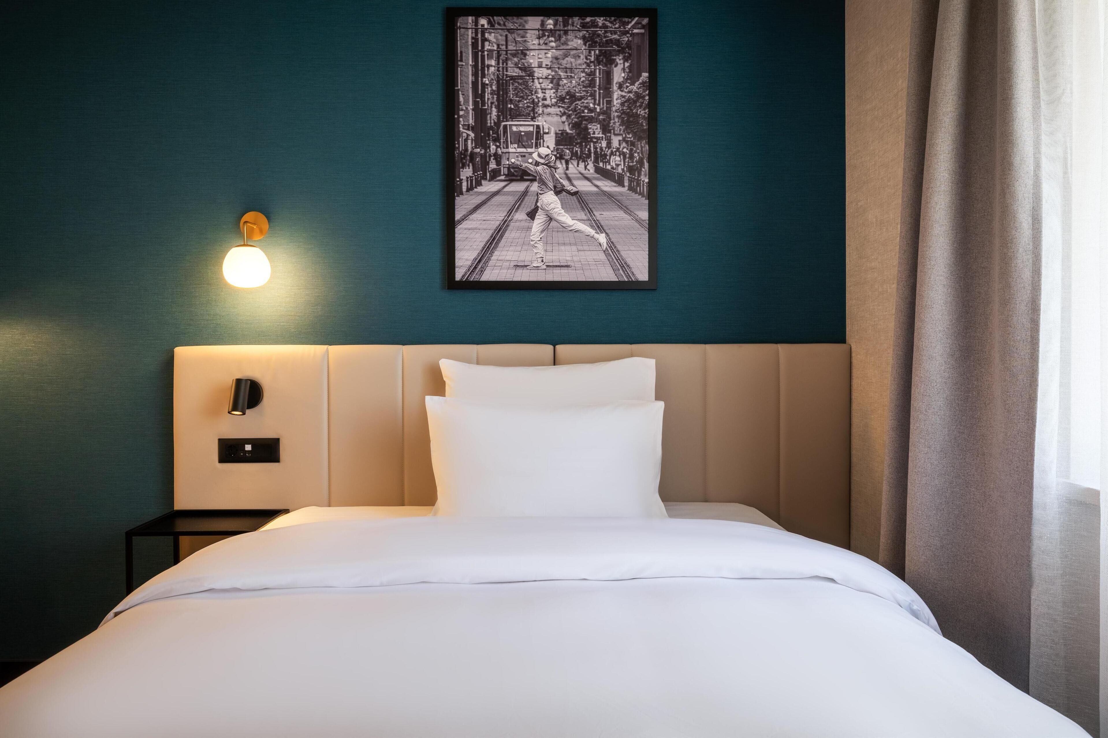 Une chambre d’hôtel avec un lit, une lampe fixée au mur, un tableau encadré et une table de chevet.