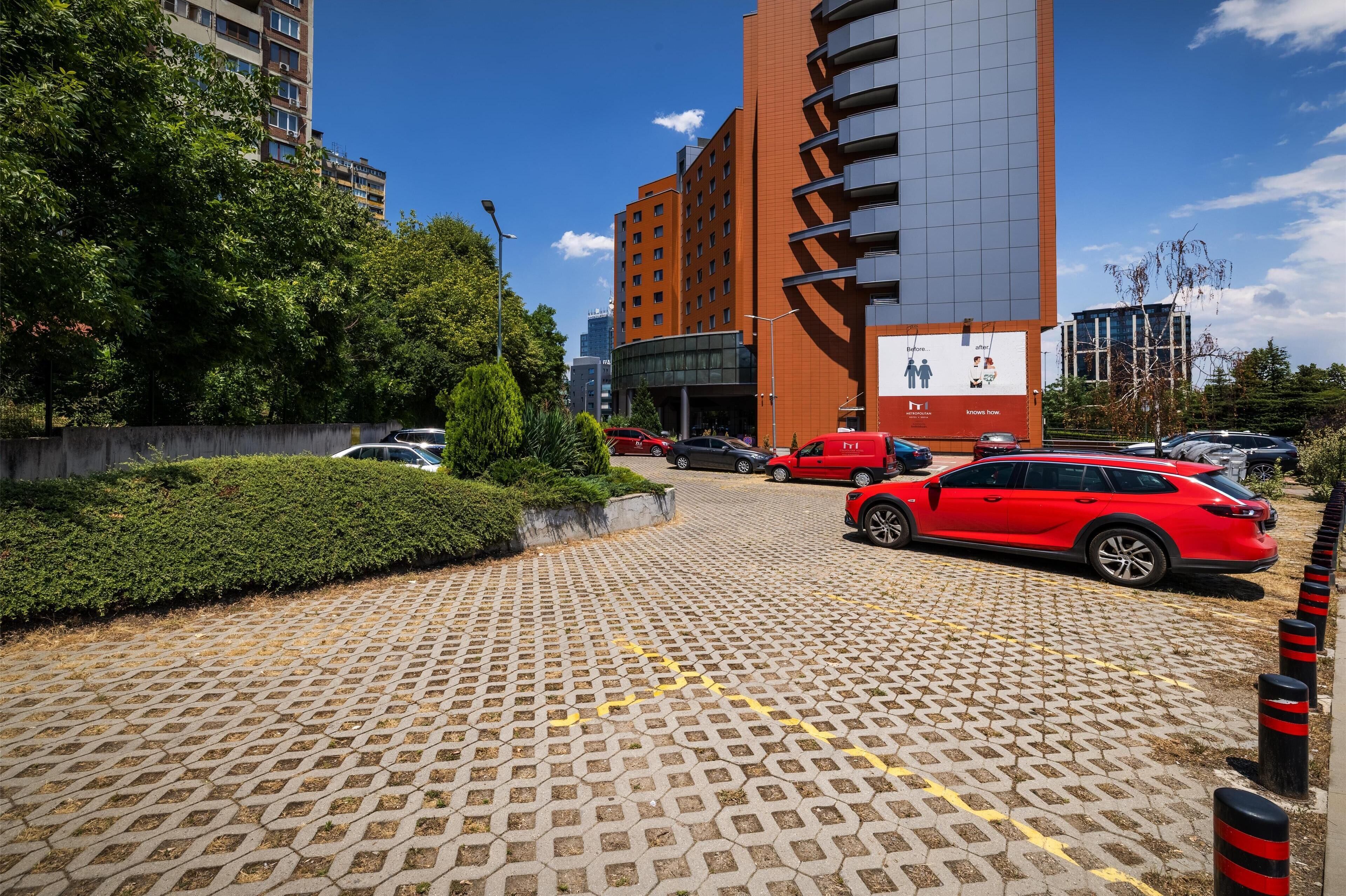 Ein Parkplatz mit einem roten Auto, befestigtem Boden und einem Gebäude mit einer Werbetafel.