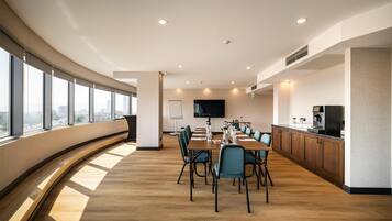 A modern conference room with a long table, chairs, a flat-screen TV, and a city view through large windows.