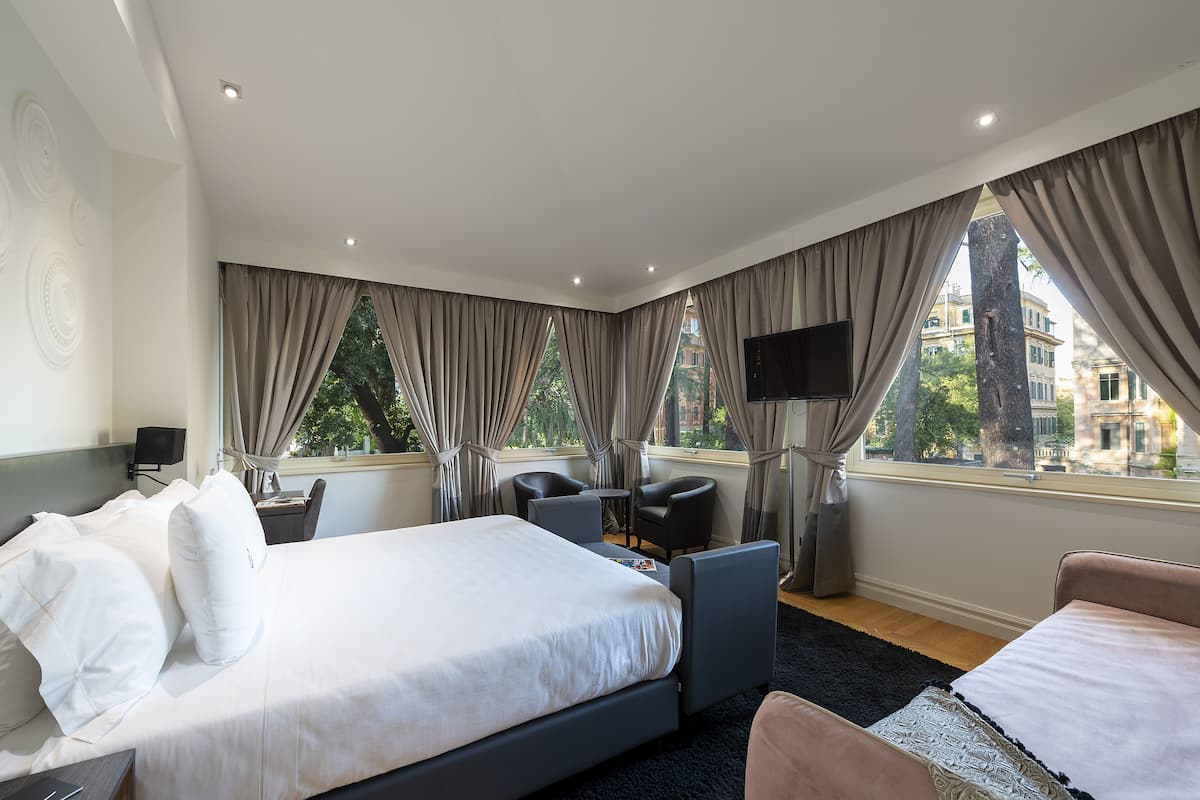 Habitación de hotel con una cama grande, dos sillones, una mesita, televisión y una ventana con cortinas.