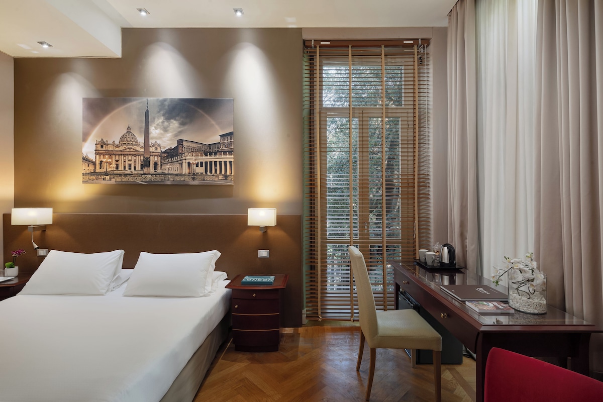 A hotel room with a large bed, two bedside lamps, a desk with a chair, a coffee maker, and a framed picture on the wall.
