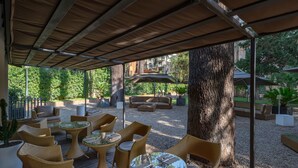 An outdoor patio area with wicker furniture, a glass table, and a seating area with cushions. - Hotel Principe Torlonia (Rome)