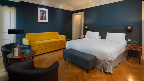A modern hotel room with a large bed, a yellow sofa, a small round table, and a black armchair. - Hotel Principe Torlonia (Rome)