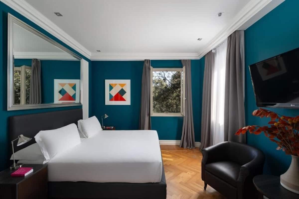 Un dormitorio con una cama, una silla, un televisor y obras de arte en las paredes.