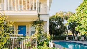 A pool area with a white fence, a blue door, and a balcony with white railings. - The Beach Club at Anna Maria by RVA (Bradenton Beach)