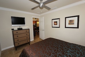 A bedroom with a bed, dresser, TV, ceiling fan, and two framed pictures on the wall.