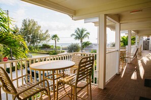 A covered outdoor area with a table and chairs, a railing, and a view of the ocean and greenery. - The Beach Club at Anna Maria by RVA (Bradenton Beach)
