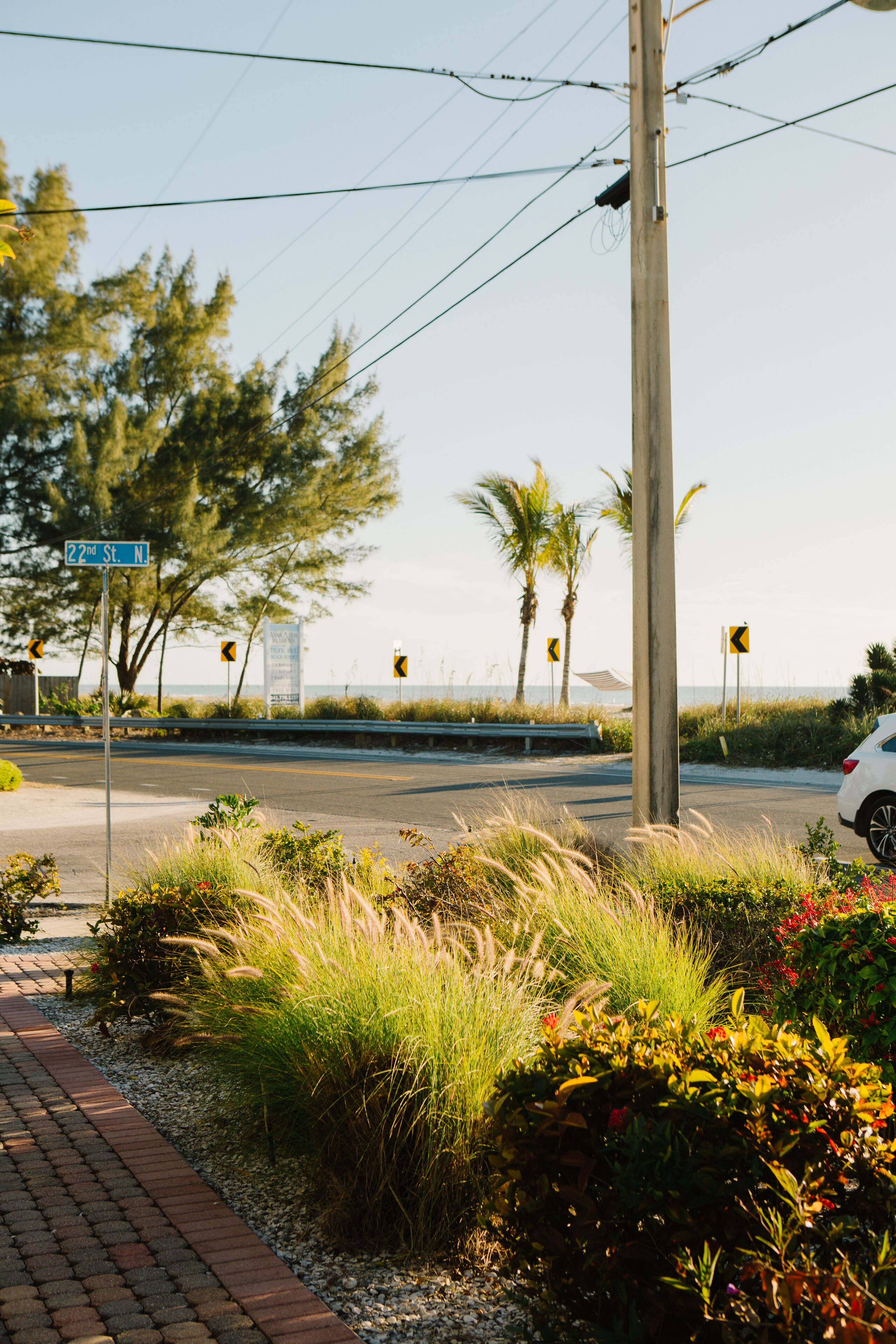 A street corner with a road sign for 22nd St. N, a white car parked on the side, and a sidewalk with plants and a brick path.