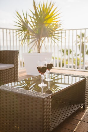 A glass table with two wine glasses, a wicker chair, and a potted plant in the background.