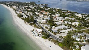 An aerial view of a coastal town with a beach, residential buildings, and a road. - The Beach Club at Anna Maria by RVA (Bradenton Beach)