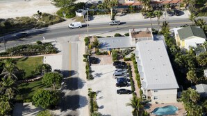 An aerial view of a coastal area with a beach, a parking lot, and buildings with a swimming pool. - The Beach Club at Anna Maria by RVA (Bradenton Beach)