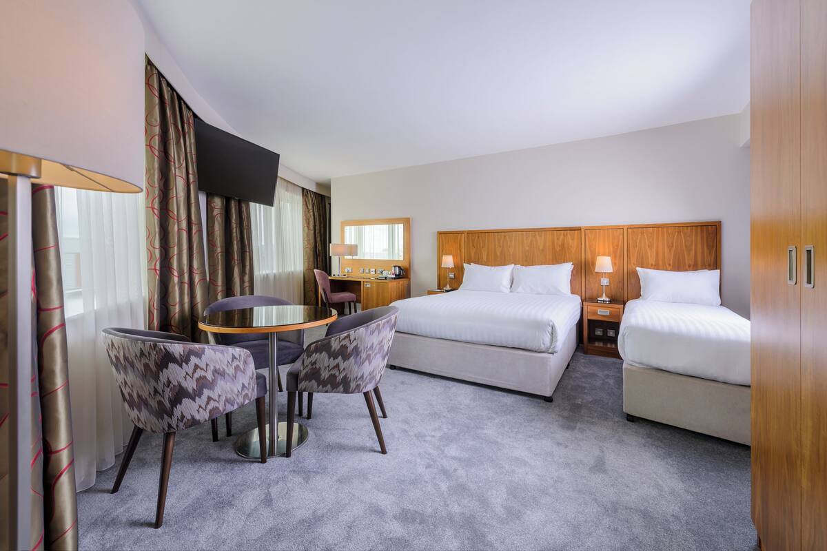 A hotel room with a bed, a desk, a chair, a TV, and a lamp.