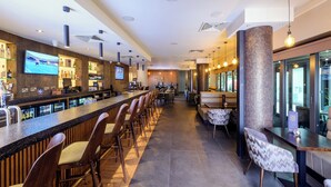 A modern bar area with a long counter, multiple bar stools, and a seating area with tables and chairs.